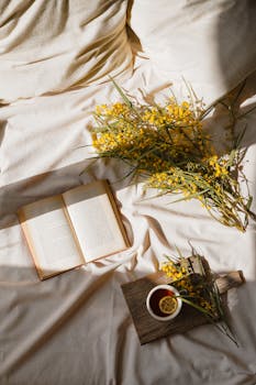 Relaxing scene with a book, cup of tea, and yellow flowers in warm sunlight.