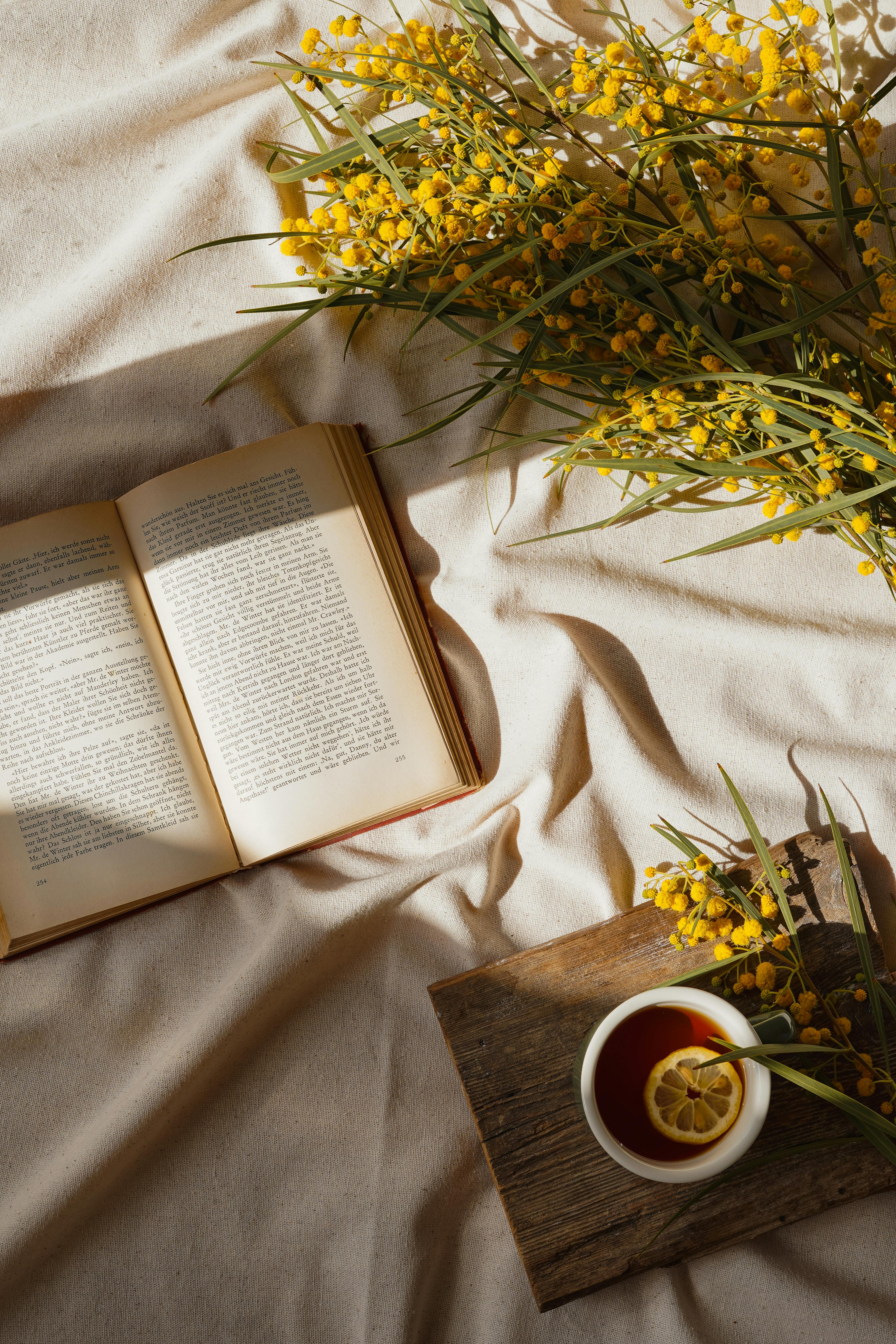 An inviting setup featuring an open book, a cup of tea, and vibrant yellow flowers.