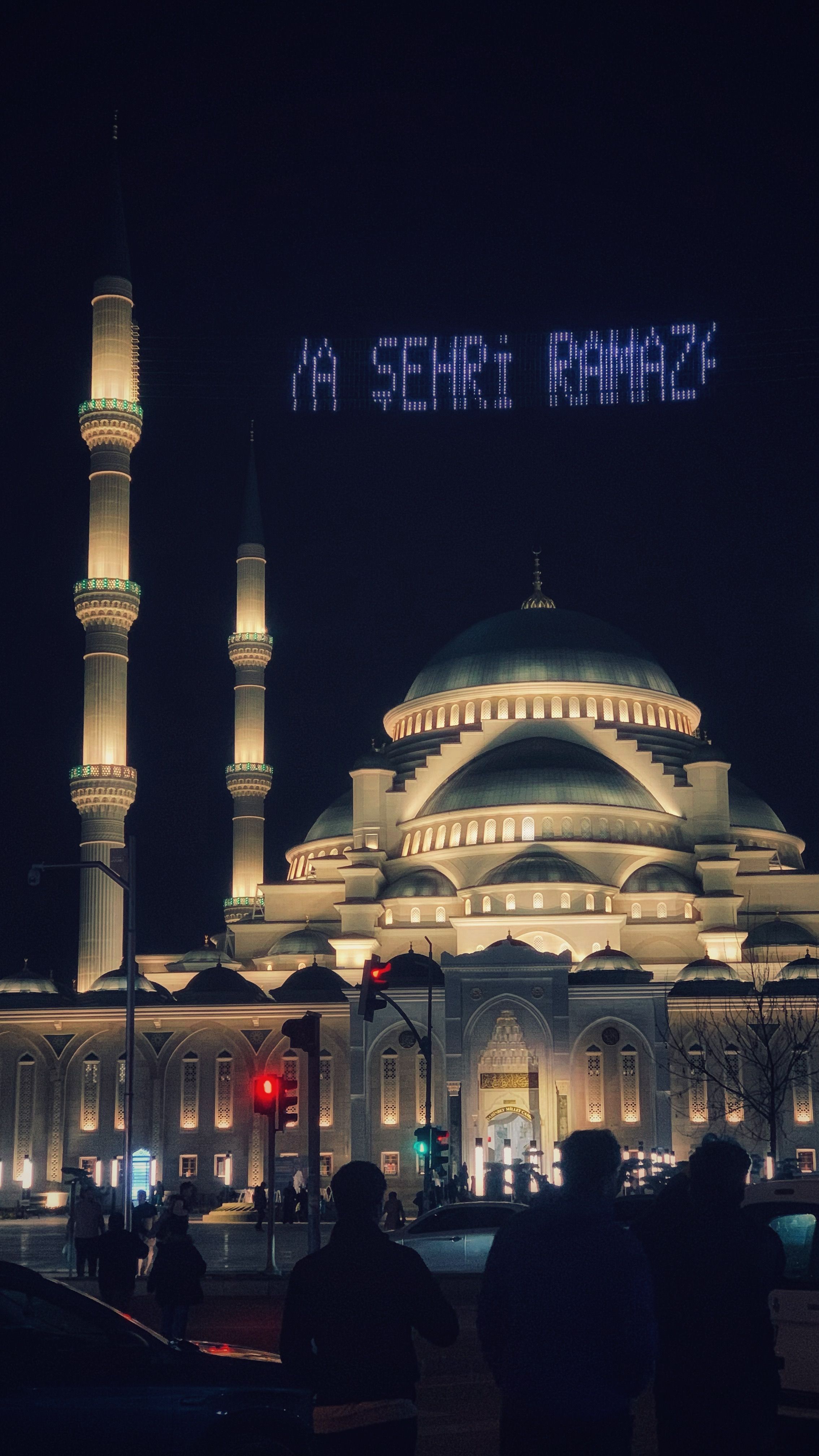 Illuminated mosque at night in Turkey with digital text in the sky.