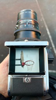 A vintage camera displays a reflection of a basketball hoop in its viewfinder.