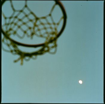 Blurred basketball hoop with sky and moon, creating an artistic view.