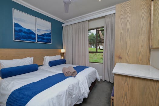 Stylish modern bedroom with blue accents, featuring double beds, art, and natural light.