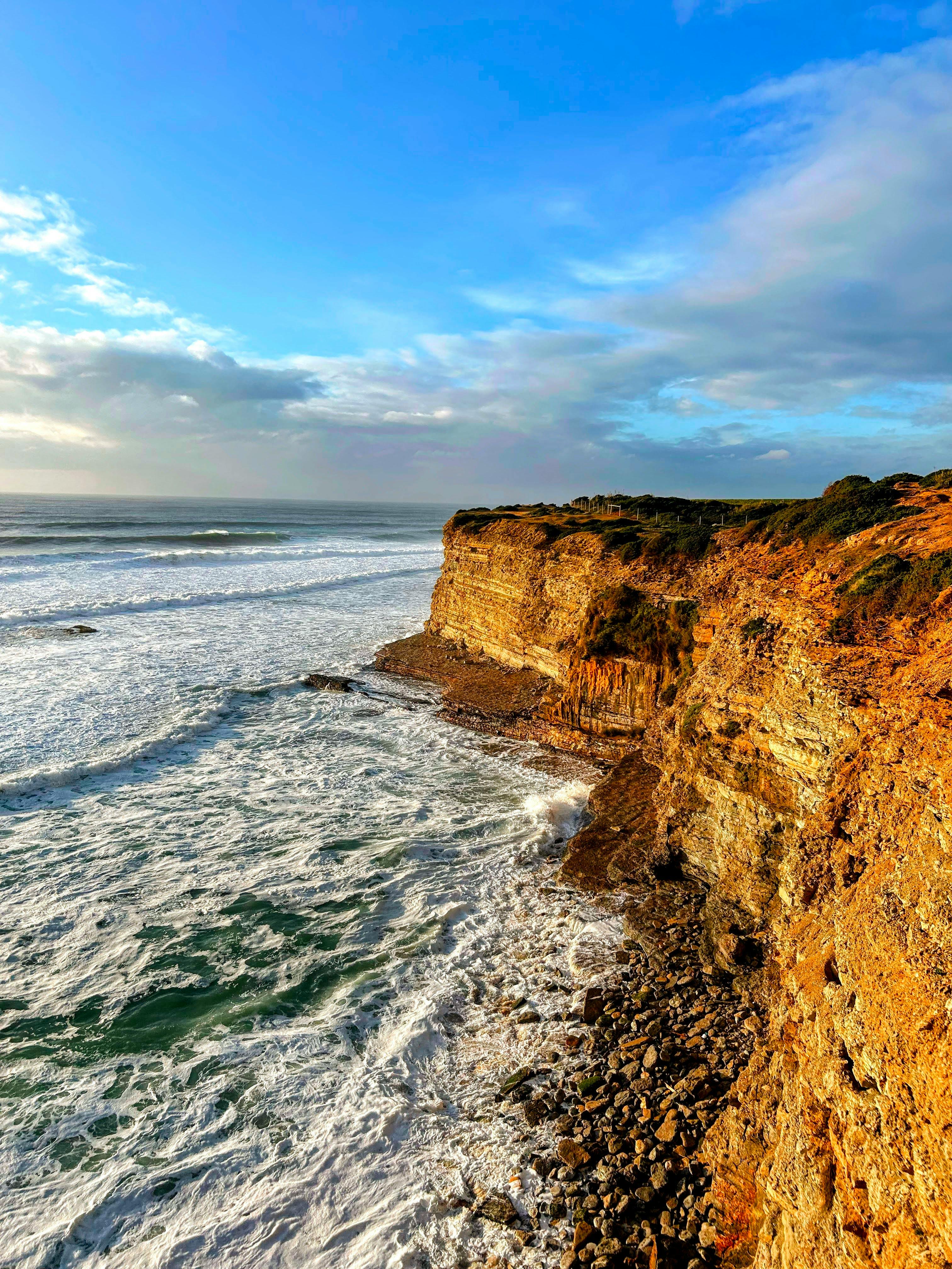 Stunning cliffside waves against a rugged coastline in Portugal at sunset.
