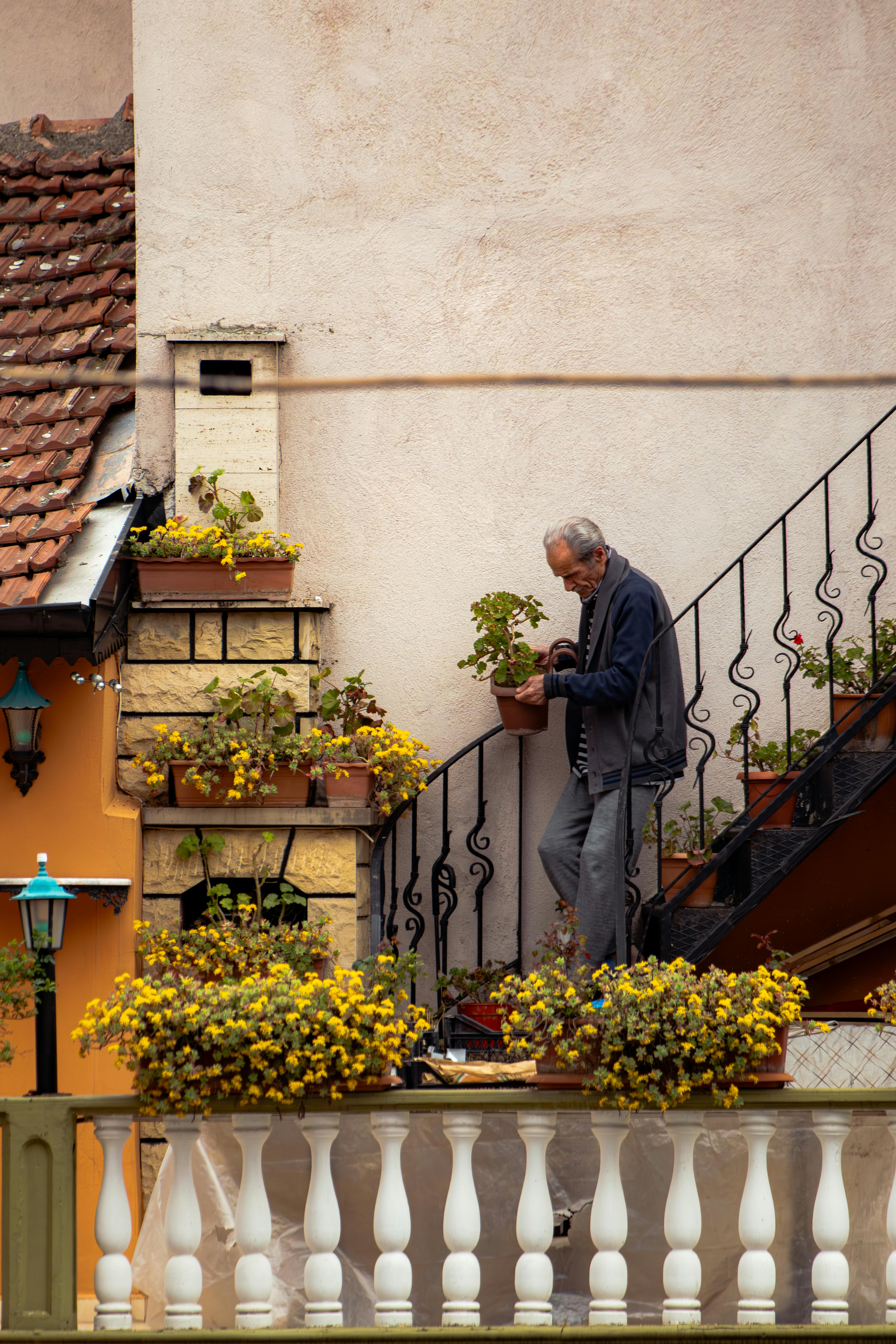 Elderly man caring for plants on balcony in Bursa, Türkiye, with rustic decor.