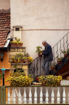 Elderly man caring for plants on balcony in Bursa, Türkiye, with rustic decor.