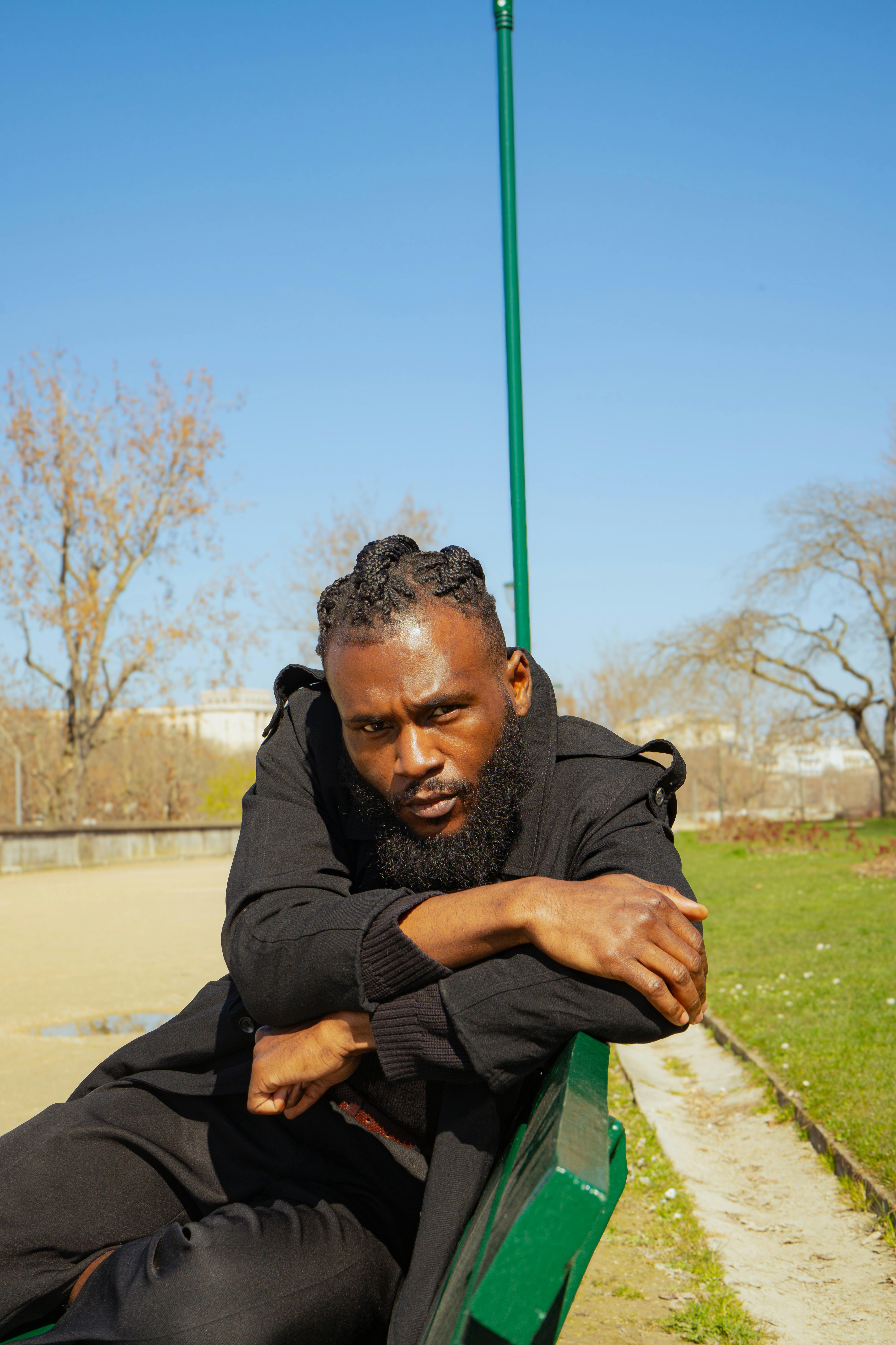 Casual portrait of a man sitting outdoors on a park bench in sunny weather.