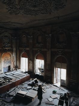 一个人站在一座黑暗的废弃建筑废墟中，建筑的拱门和天花板装饰华丽