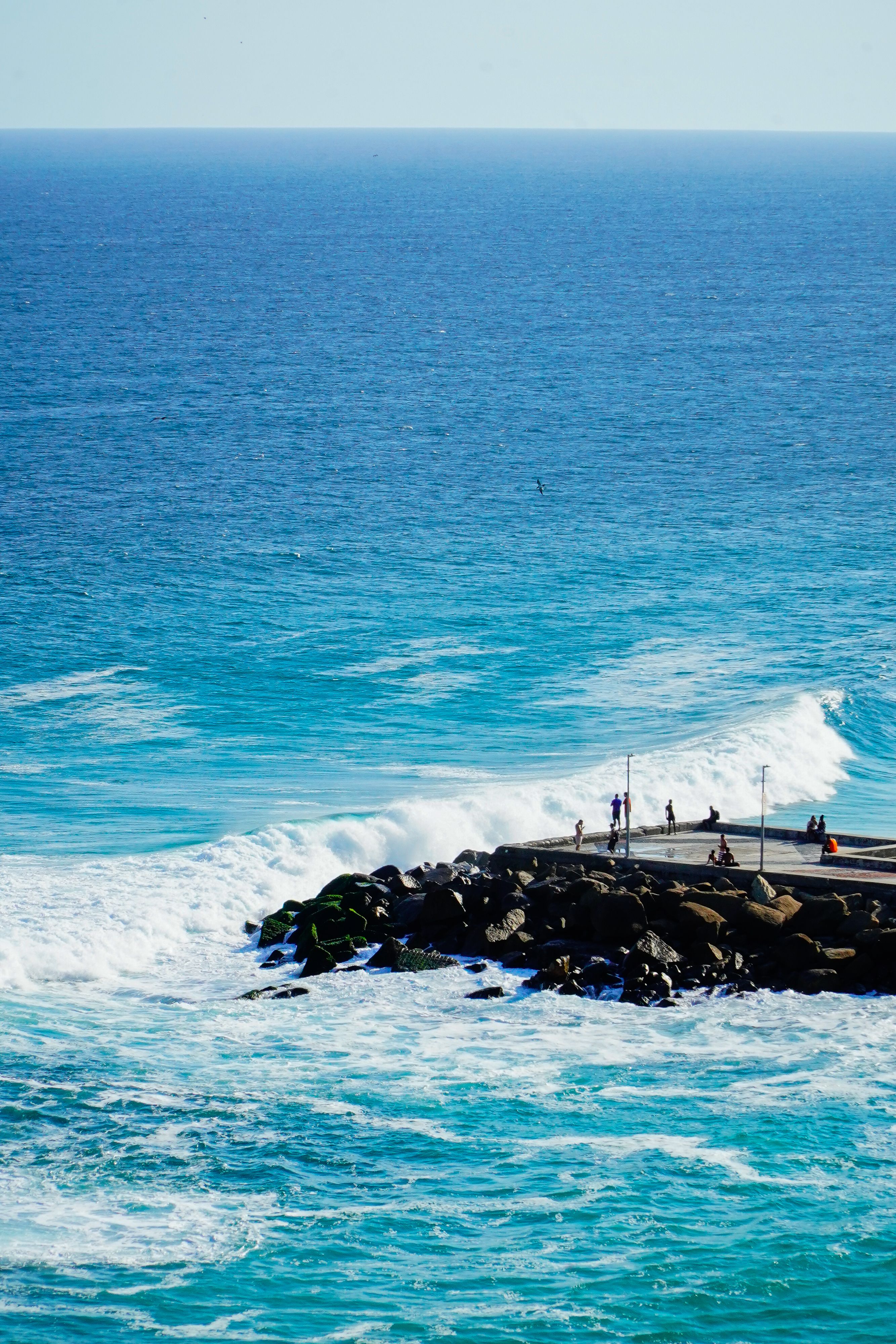 A vibrant ocean scene with a rocky jetty and people enjoying the coastal view.