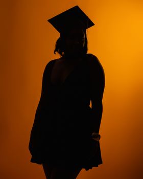 Artistic silhouette of a graduate in cap and gown on a vibrant orange background.
