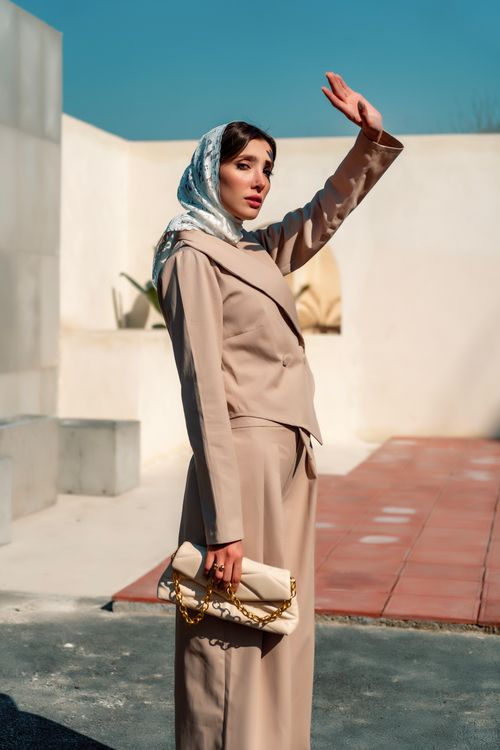 Free Fashionable woman in beige outfit waving under clear sky. Stock Photo