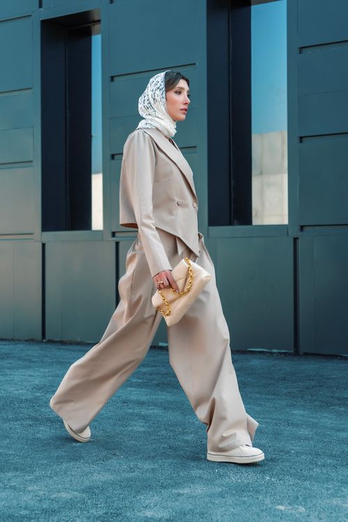 Free Elegant woman wearing a beige suit and headscarf walking by a modern building. Stock Photo