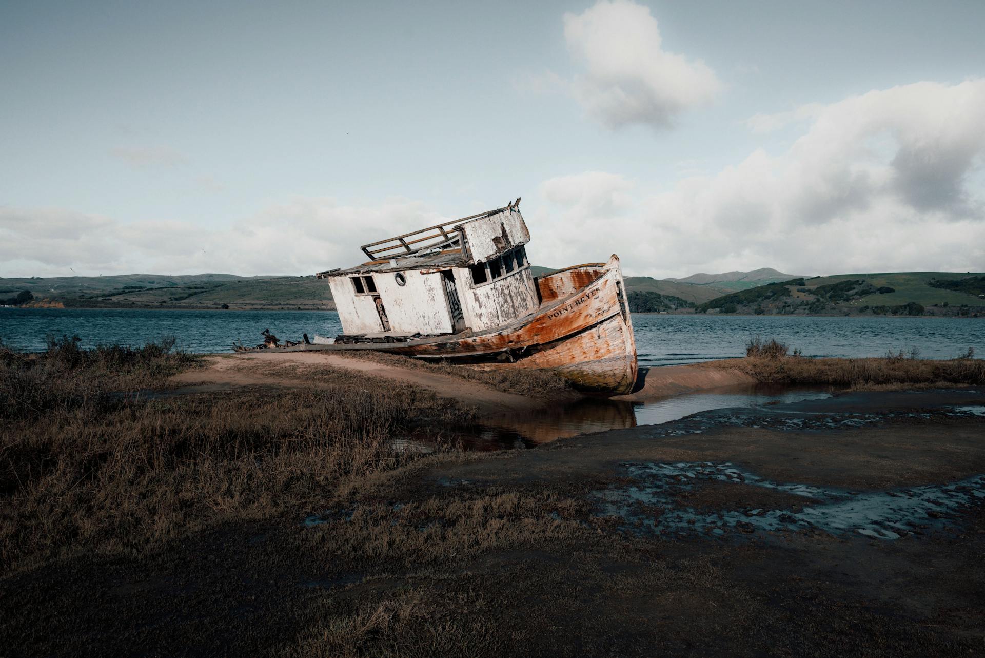 A sunken ship rests on the shore with tranquil waters and light clouds at dawn.