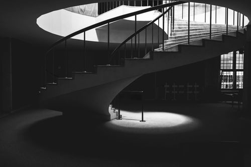 Free Artistic black and white photo of a spiral staircase with dramatic lighting. Stock Photo
