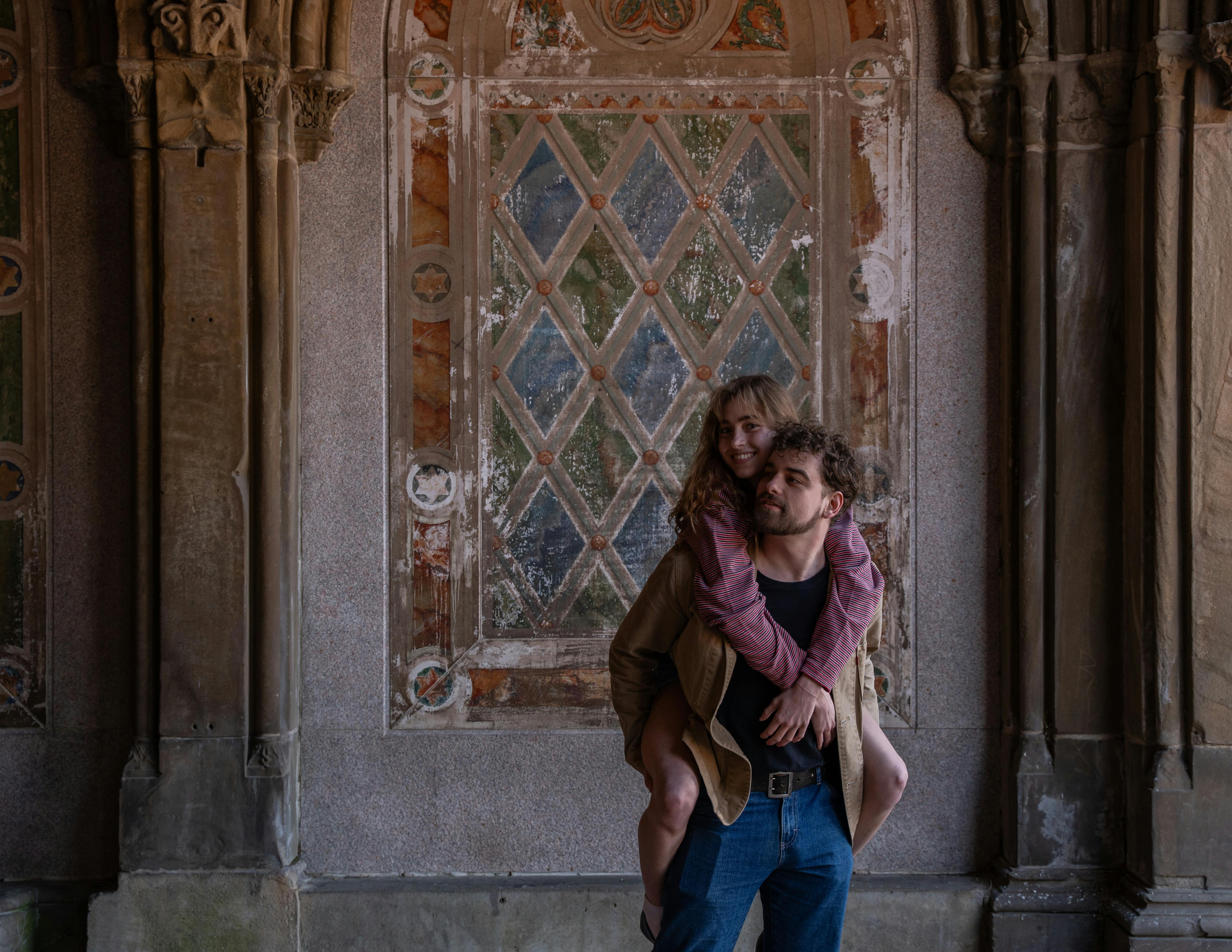 A couple shares a joyful moment in Central Park, NYC, against a historic backdrop.