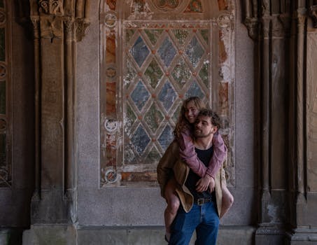 A couple shares a joyful moment in Central Park, NYC, against a historic backdrop.