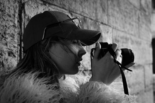 Free A woman in a cap takes a photograph with a camera against a stone wall. Stock Photo