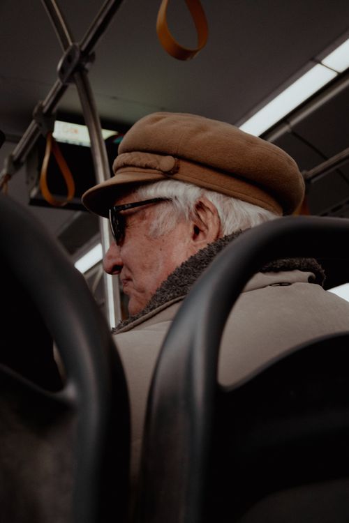 Free Senior adult wearing a hat sitting on a bus. Captured in a candid moment. Stock Photo