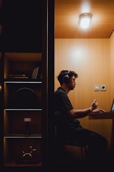 Young man wearing headphones working intently on laptop in a warm-toned, modern workspace.