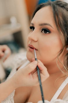 A makeup artist skillfully applies lipstick to a bride's lips, focusing on detail.