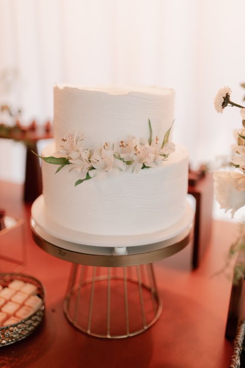 Free Two-tier white wedding cake adorned with fresh flowers on a stylish stand. Stock Photo