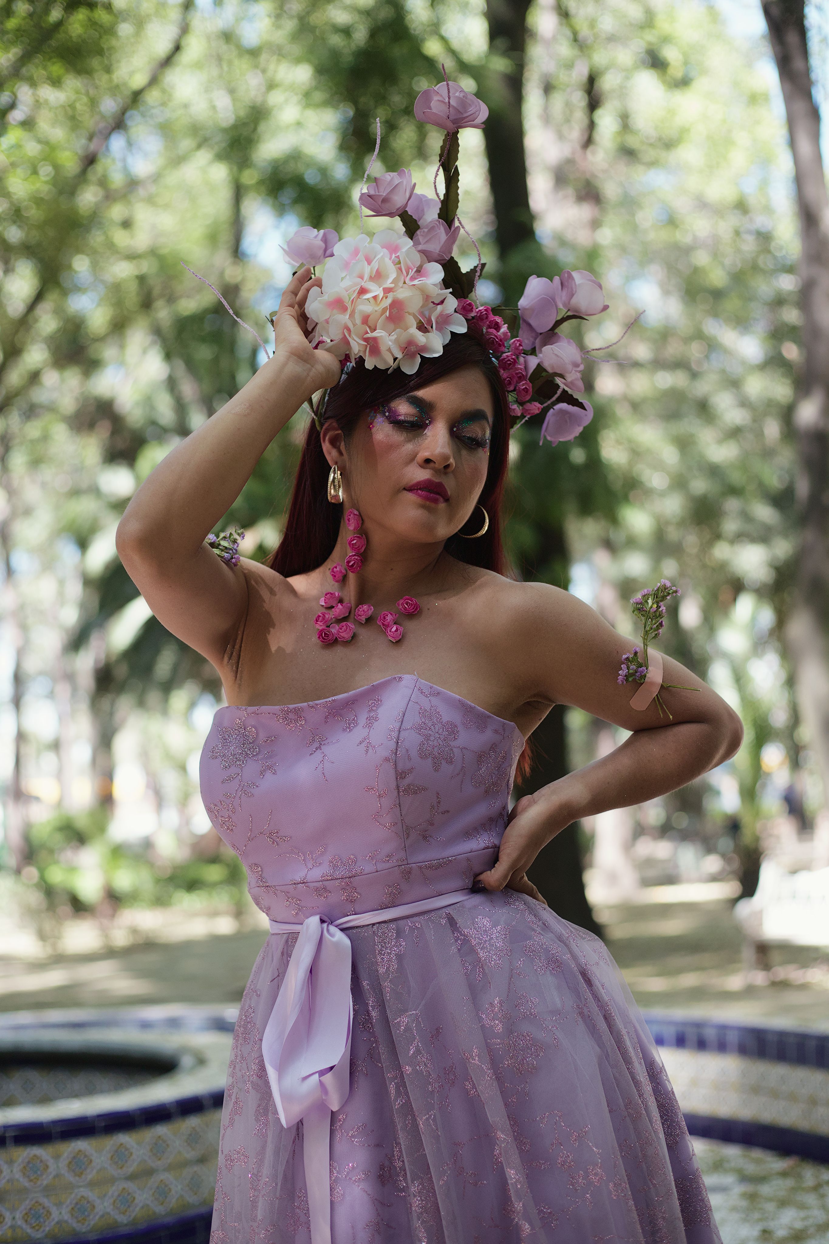 Fotomural Una mujer con un vestido lavanda y un tocado floral posa con gracia en un parque soleado.