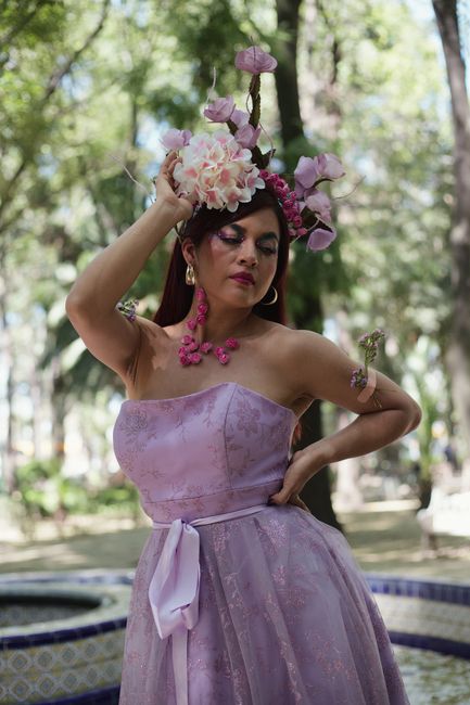 Fotomural Una mujer con un vestido lavanda y un tocado floral posa con gracia en un parque soleado.
