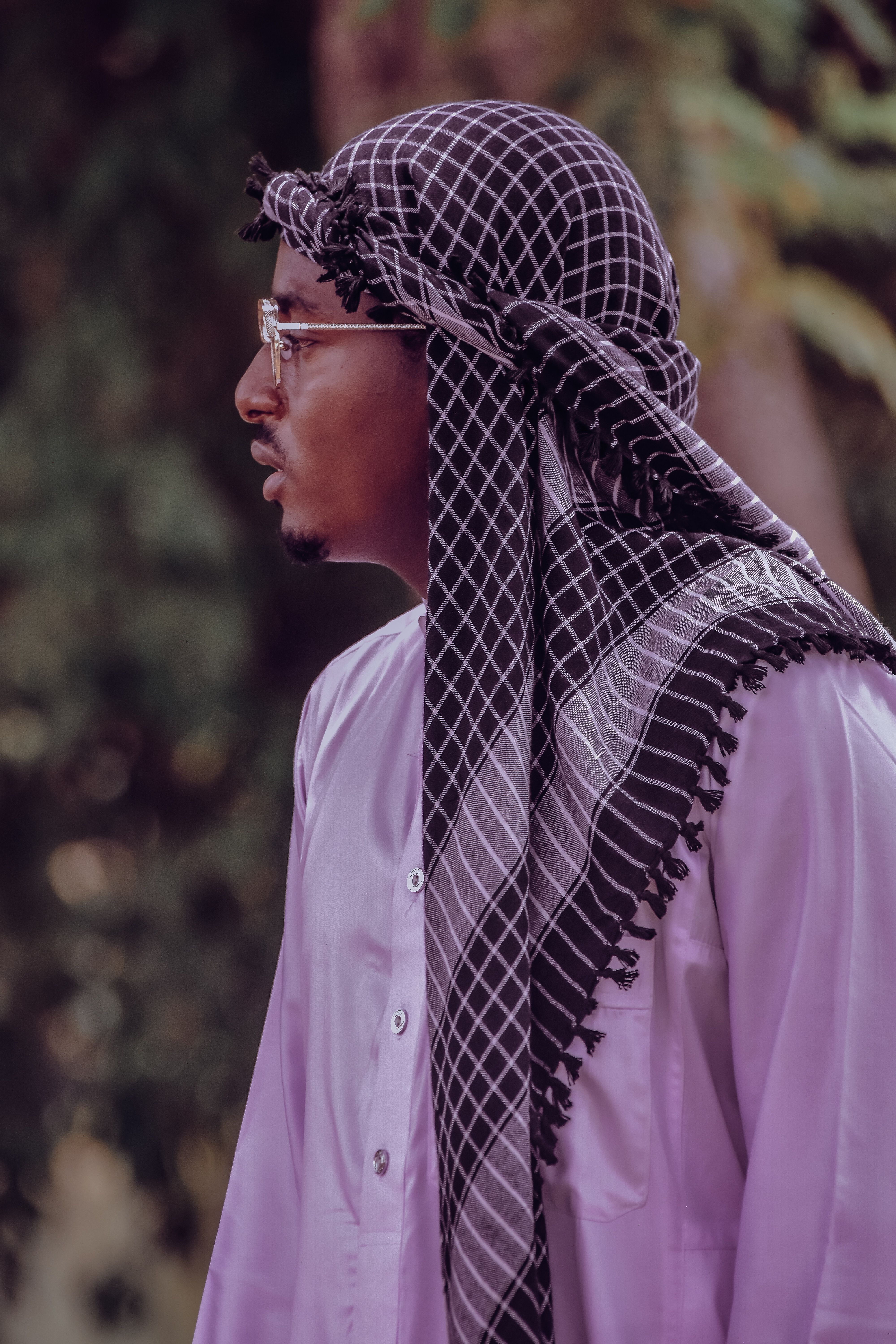 A man wearing a purple shirt and traditional headscarf standing outdoors.