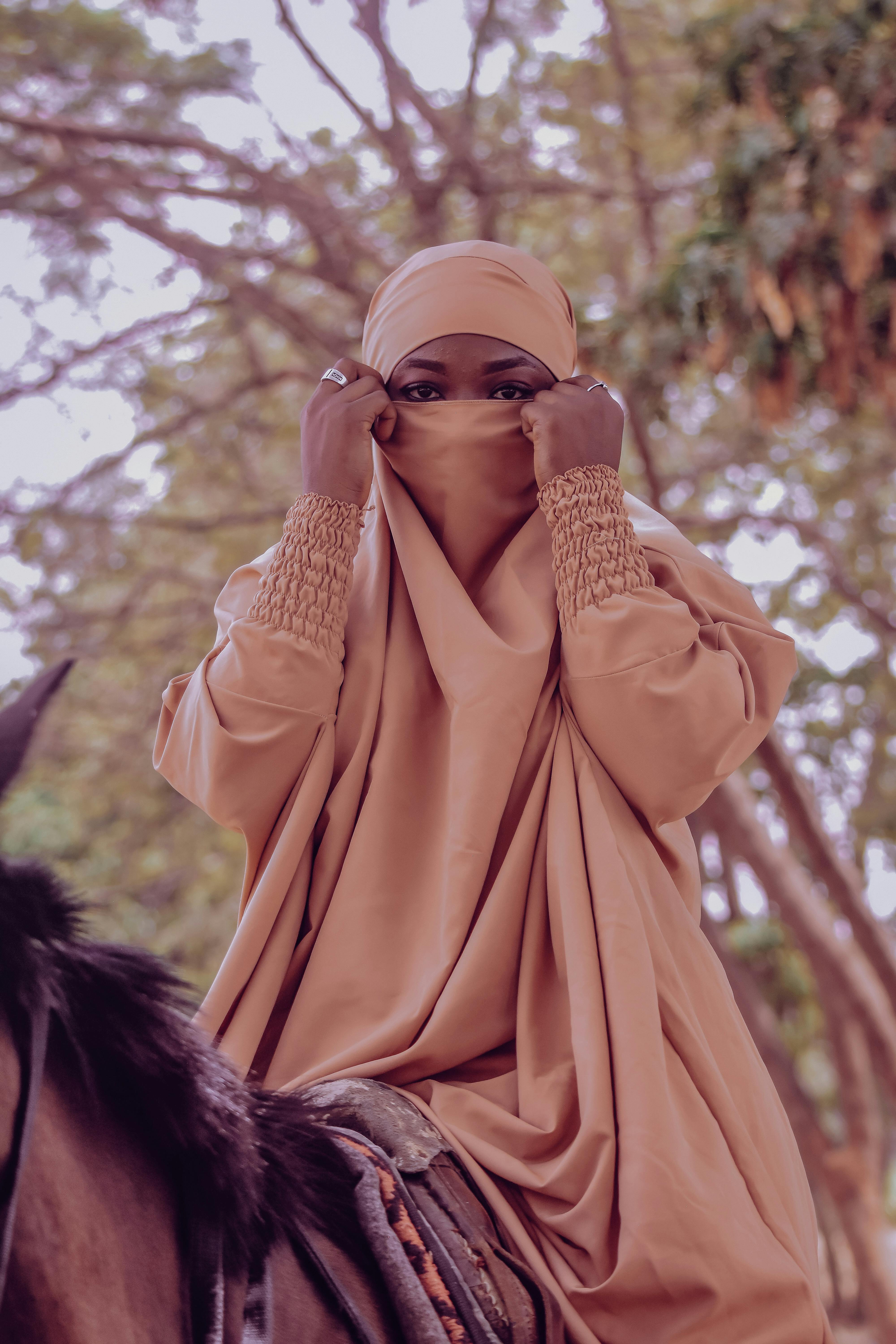 Free A woman in traditional attire poses on horseback amidst lush greenery, embodying cultural elegance. Stock Photo