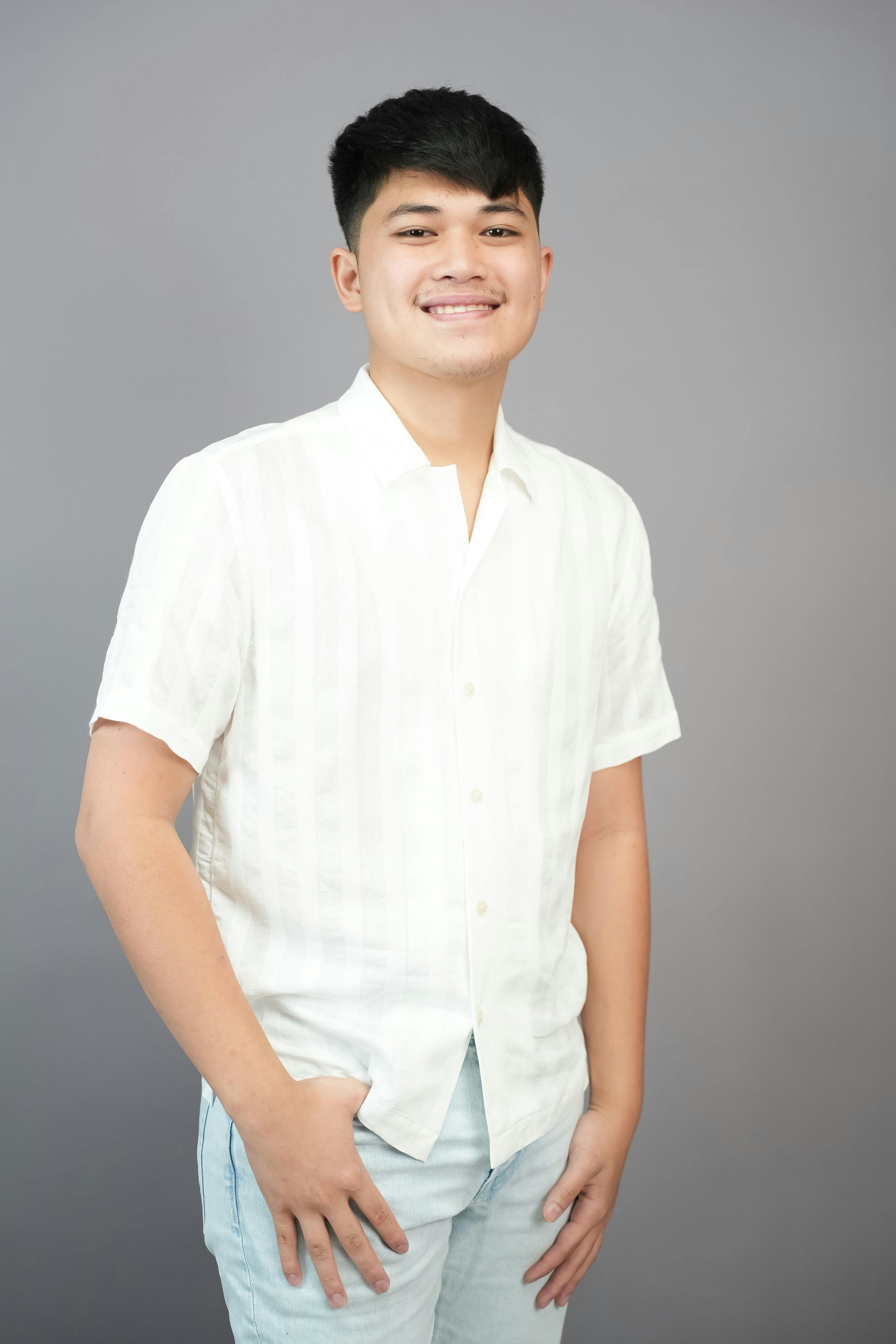 Smiling young adult in casual white shirt against gray background.