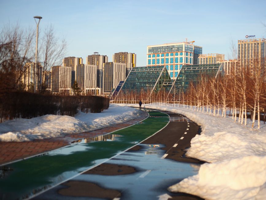 Astana in winter features modern buildings and a snowy urban park.