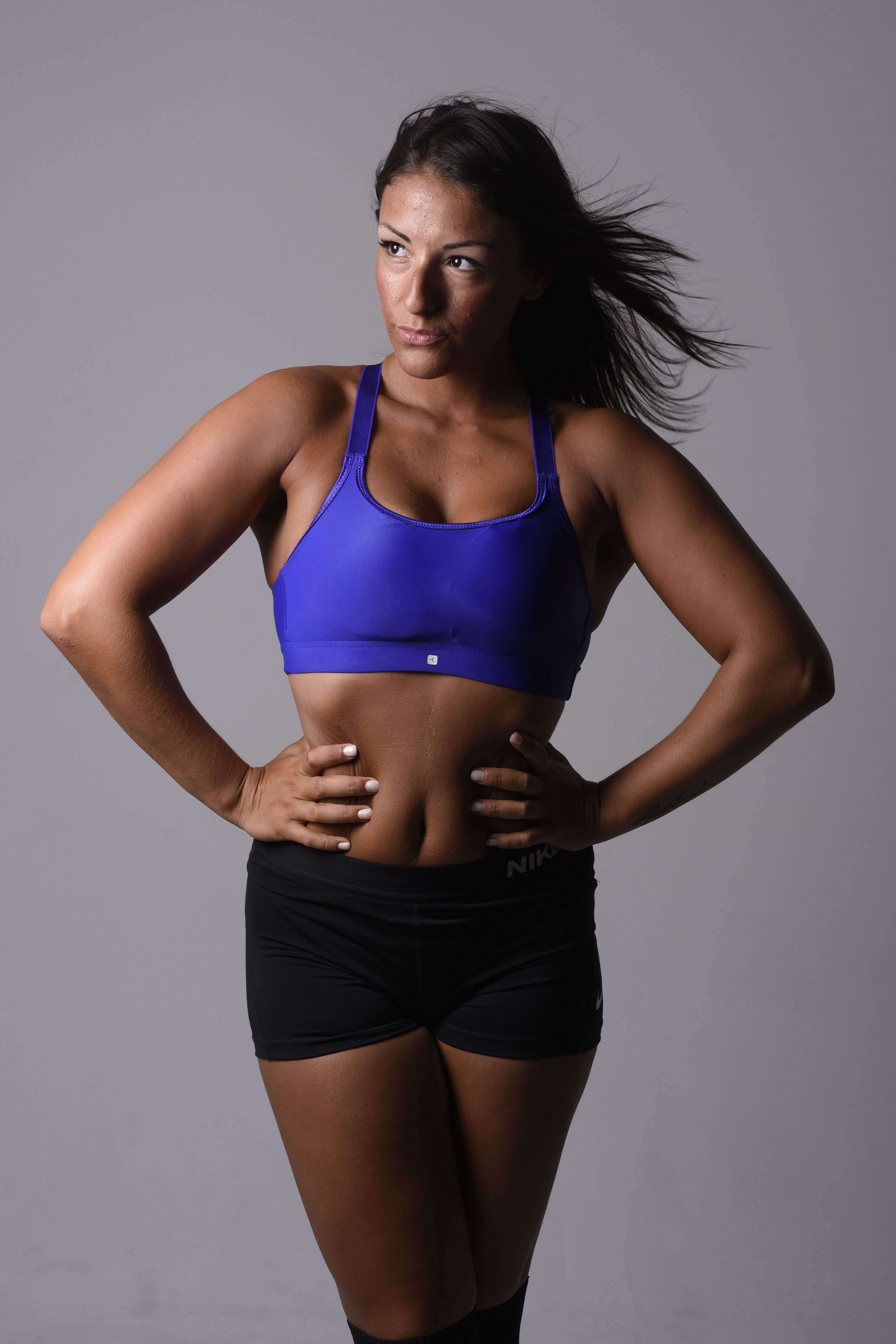 Strong athletic woman in sportswear posing confidently against a neutral background.
