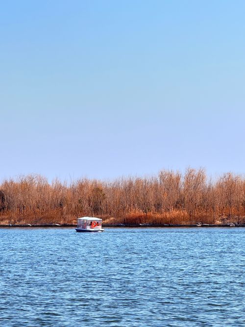 Free A peaceful autumn scene with a small boat on a lake, surrounded by trees. Stock Photo