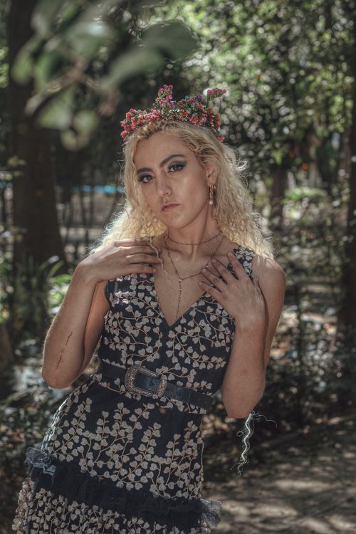 Free A woman in a floral dress and crown poses confidently outdoors, embodying natural elegance. Stock Photo