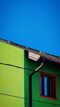 A bright green house with contrasting red window frames and a clear blue sky backdrop.