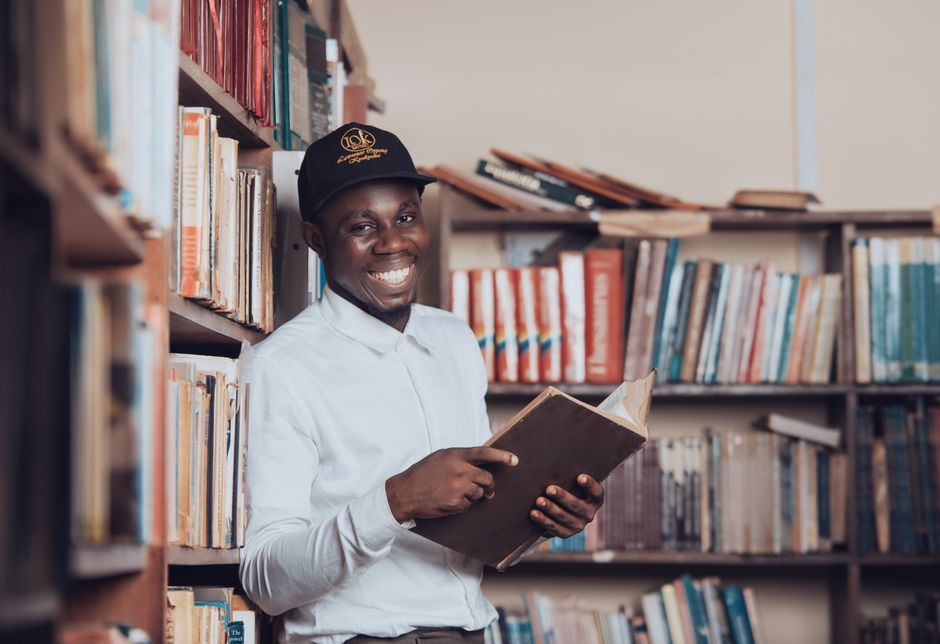 A joyful man reading in a Ghanaian library, symbolizing education and knowledge.