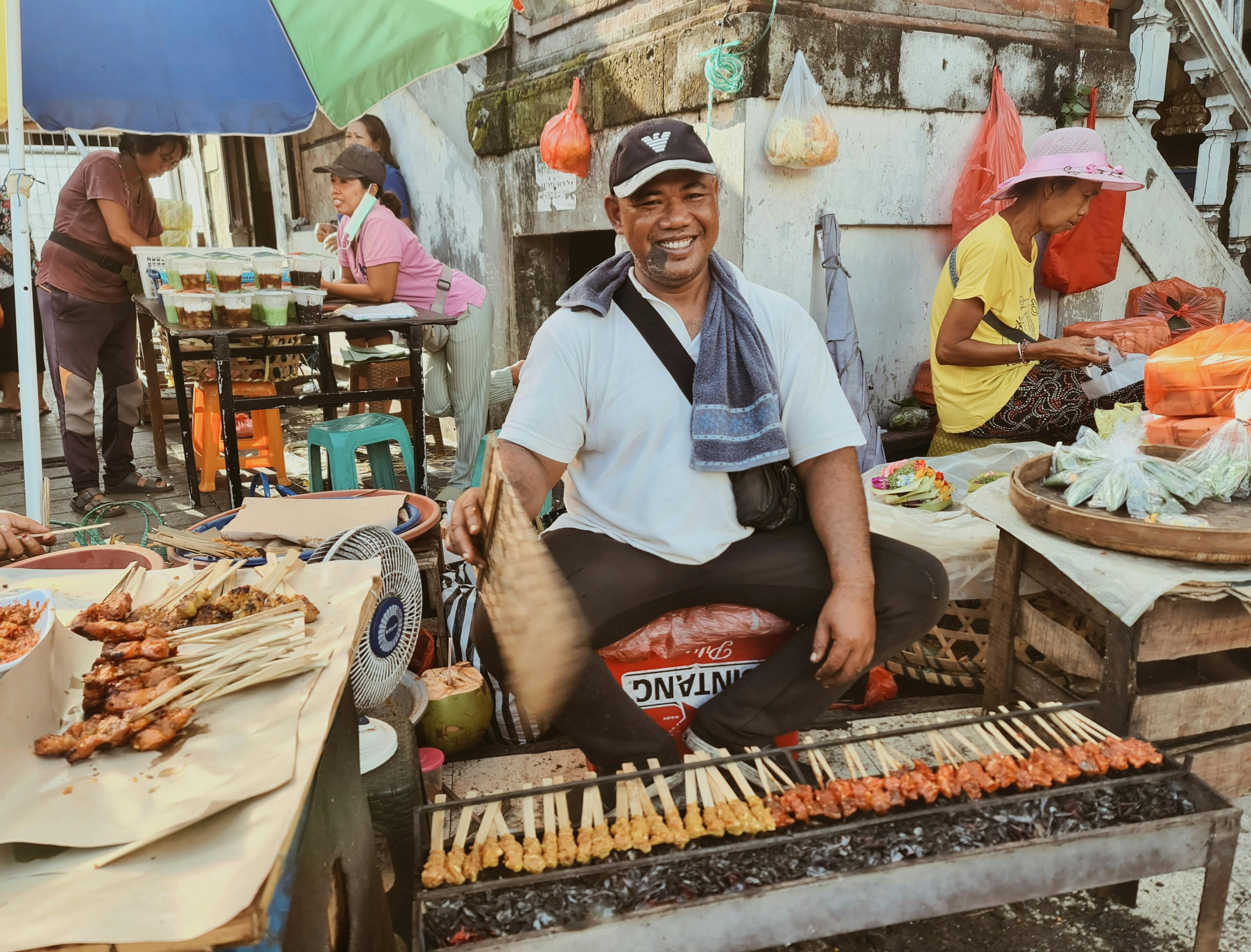 Joyful vendor grilling satay at a lively Bali street food market.