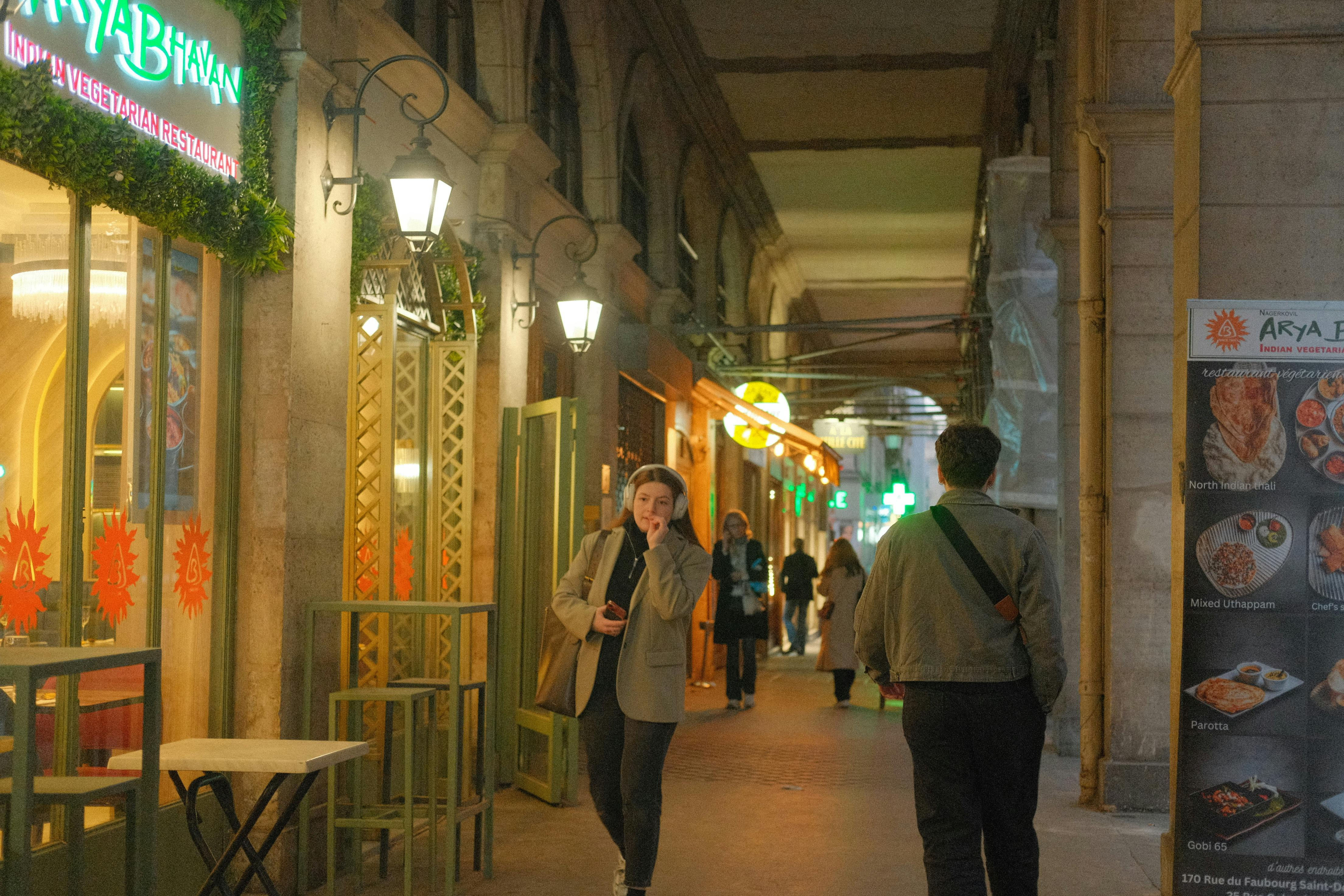 Nighttime alley street with Indian restaurant and people walking.