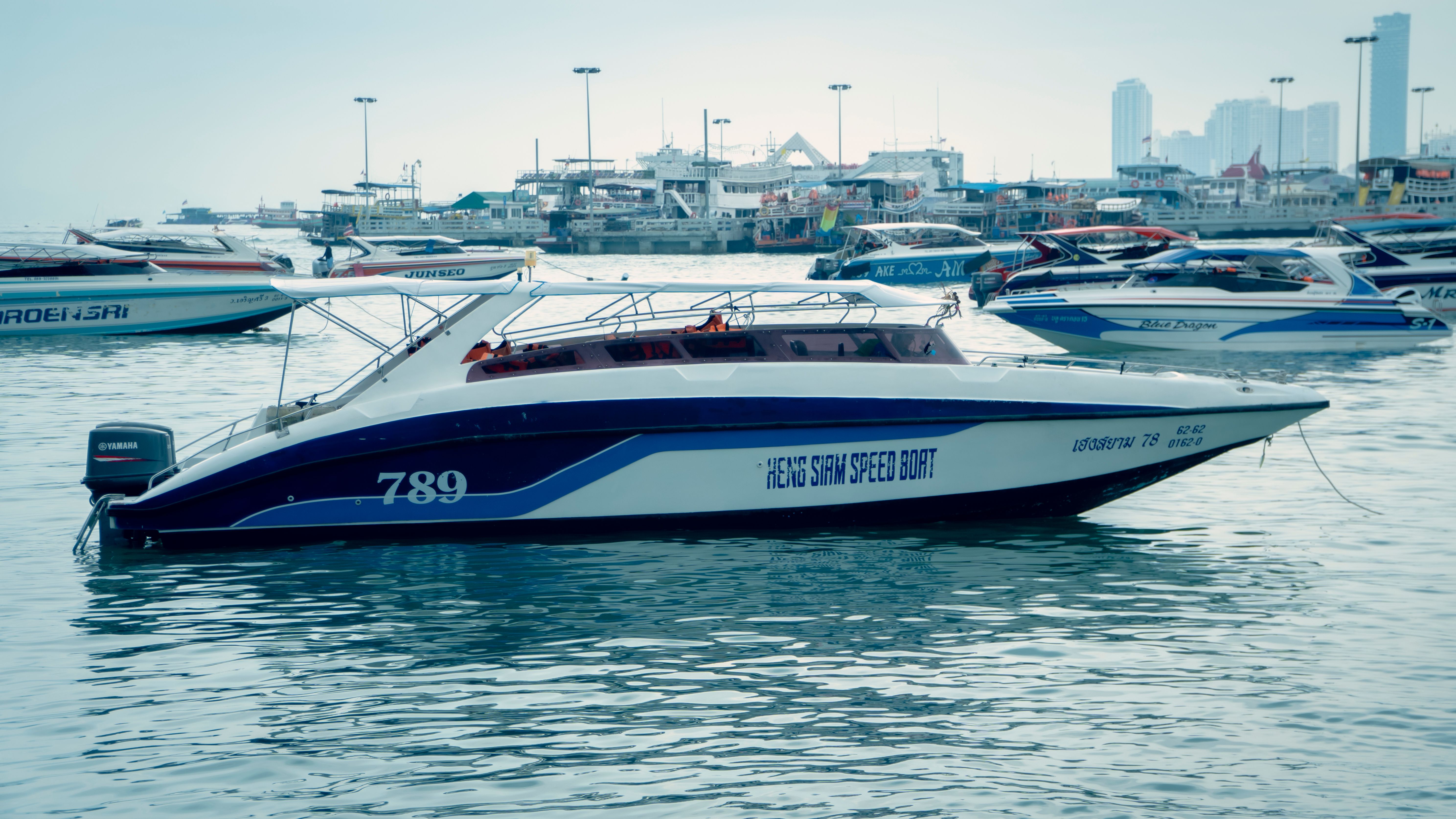 A speedboat moored in a busy marina, surrounded by other boats with a cityscape in the background.