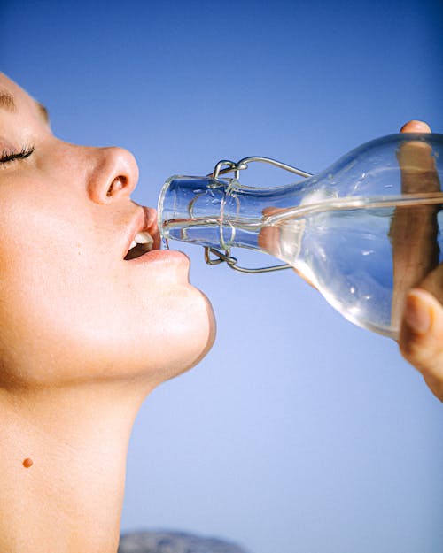 Женщина пьет воду из стеклянной бутылки