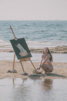 A woman painting on the beach, capturing serene summer vibes.