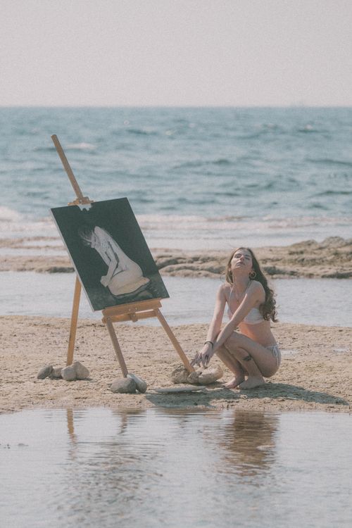 Free A woman painting on the beach, capturing serene summer vibes. Stock Photo