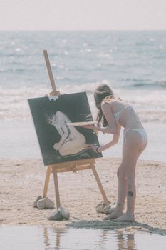 A woman in bikini paints on the beach near the ocean. Serene summer day with waves crashing gently.