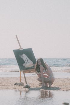 A woman painting on a beach during a sunny day, creating art amidst serene ocean waves.