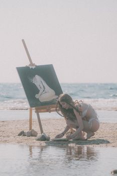Woman in bikini painting on a beach by the sea, capturing tranquility.