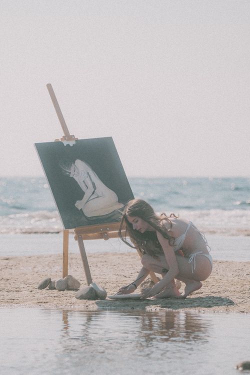 Free Woman in bikini painting on a beach by the sea, capturing tranquility. Stock Photo