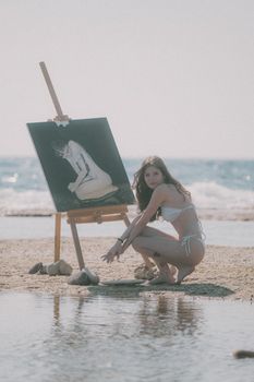 Woman in bikini painting on the beach, blending art and nature in serene harmony.