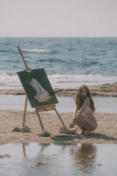 A woman paints by the beach, capturing a serene scene under bright sunlight.