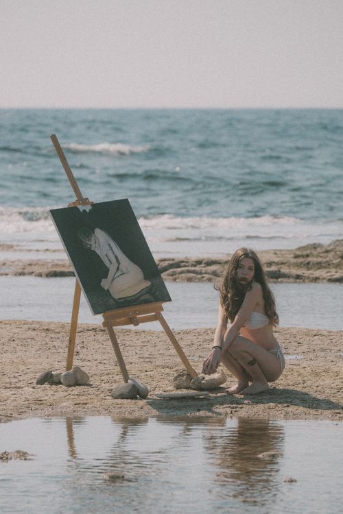 Free A woman paints by the beach, capturing a serene scene under bright sunlight. Stock Photo