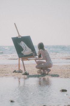 A woman painting on a beach easel captures the serene ocean view under sunlight.