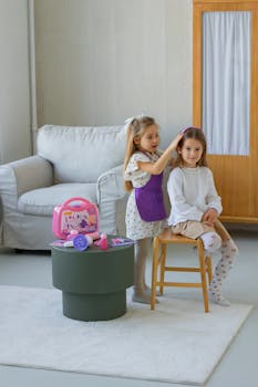 Two young girls role-playing as hairdresser and client in a cozy living room setting.